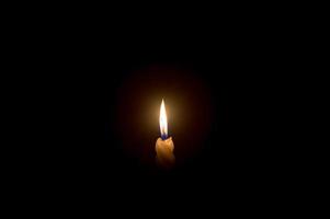 una sola llama de vela encendida o luz que brilla en una vela blanca en espiral sobre fondo negro u oscuro en la mesa de la iglesia para Navidad, funeral o servicio conmemorativo foto