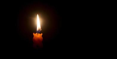 A single burning candle flame or light glowing on an orange candle on black or dark background on table in church for Christmas, funeral or memorial service with copy space photo