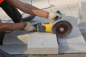 Hands of worker with electric grinder trims paving slabs on the construction site. Concept of laying new sidewalk tile. Stone cutting equipment. Road works. Civil engineering. Repair asphalt. Close-up photo