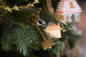 Key to the house with a keychain is hanging on the Christmas tree. A gift for New Year, Christmas. Building, design, project, moving to new house, mortgage, rent and purchase real estate. Copy space photo