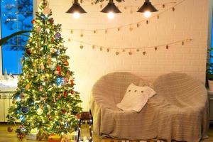 árbol de navidad en el interior blanco de una casa con paredes de ladrillo estilo loft con guirnaldas de juguetes de vidrio en una cuerda. decoración de luces de hadas brillantes de la sala de estudio. hogar acogedor en navidad y año nuevo foto