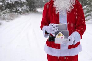 llave de la casa con llavero cabaña en manos de santa claus al aire libre en la nieve. trato de bienes raíces, compra, construcción, reubicación, hipoteca. hogar acogedor. feliz navidad, evento de reserva de año nuevo y sala foto