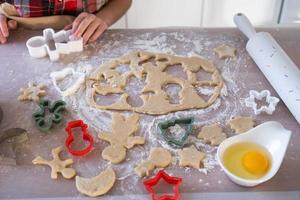 las manos de mamá e hija recortan galletas de la masa con moldes sobre un tema navideño en forma de muñeco de nieve, árbol de navidad, estrellas foto