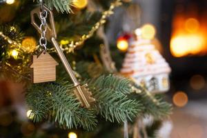 Key to the house with a keychain is hanging on the Christmas tree. A gift for New Year, Christmas. Building, design, project, moving to new house, mortgage, rent and purchase real estate. Copy space photo