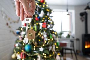 la llave de la casa con un llavero está colgada en el árbol de navidad. un regalo para año nuevo, navidad. construcción, diseño, proyecto, mudanza a casa nueva, hipoteca, alquiler y compra de bienes inmuebles. copie el espacio foto