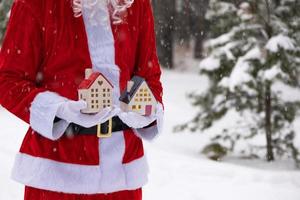 llave de la casa con llavero cabaña en manos de santa claus al aire libre en la nieve. trato de bienes raíces, compra, construcción, reubicación, hipoteca. hogar acogedor. feliz navidad, evento de reserva de año nuevo y sala foto