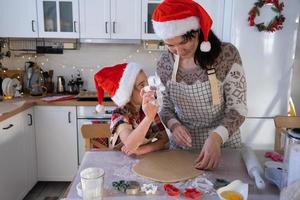 Mom and daughter in the white kitchen are preparing cookies for Christmas and new year. Family day, preparation for the holiday, learn to cook delicious pastries, cut shapes out of dough with molds photo