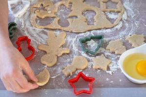 las manos de mamá e hija recortan galletas de la masa con moldes sobre un tema navideño en forma de muñeco de nieve, árbol de navidad, estrellas foto