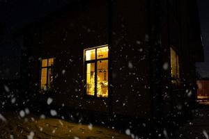 Cozy festive window of the house outside with the warm light of fairy lights garlands inside - celebrate Christmas and New Year in a warm home. Christmas tree, bokeh, snow on pine trees and snowfall photo