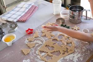 las manos de mamá e hija recortan galletas de la masa con moldes sobre un tema navideño en forma de muñeco de nieve, árbol de navidad, estrellas foto