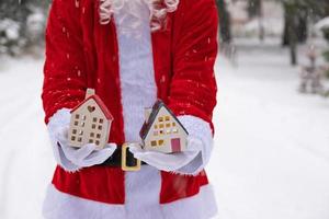 House key with keychain cottage in hands of Santa Claus outdoor in snow. Deal for real estate, purchase, construction, relocation, mortgage. Cozy home. Merry Christmas, new year booking event and hall photo