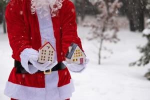 House key with keychain cottage in hands of Santa Claus outdoor in snow. Deal for real estate, purchase, construction, relocation, mortgage. Cozy home. Merry Christmas, new year booking event and hall photo