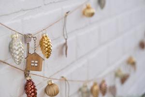 Key to house with keychain is hanging on garland of Christmas tree toys on wall. Gift for New Year, Christmas. Building, design, project, moving to new house, mortgage, rent and purchase real estate. photo