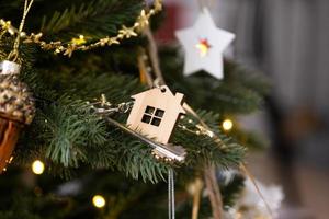 Key to the house with a keychain is hanging on the Christmas tree. A gift for New Year, Christmas. Building, design, project, moving to new house, mortgage, rent and purchase real estate. Copy space photo