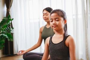 mujer entrenadora de yoga enseñando a una niña a posar y hacer ejercicio de yoga junto con su perro en casa foto