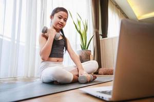 Little Girl doing dumbbell exercise by using online learning with a laptop computer at home photo