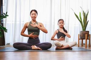 Asian mom and her girl setting prepare to yoga and meditation pose together on yoga mat at home photo