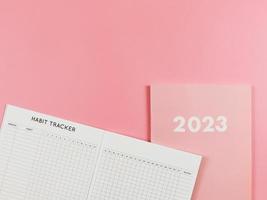 flat lay of habit tracker book on pink diary or planner 2023 on pink background with copy space. photo