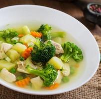 Chicken soup with broccoli, green peas, carrots and celery in a white bowl on a wooden background in rustic style photo