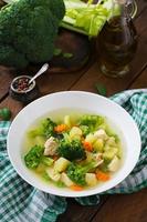 Chicken soup with broccoli, green peas, carrots and celery in a white bowl on a wooden background in rustic style photo
