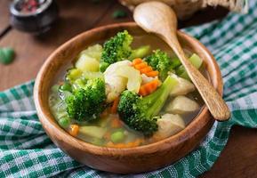 sopa de pollo con brócoli, guisantes, zanahorias y apio en un tazón sobre un fondo de madera de estilo rústico foto