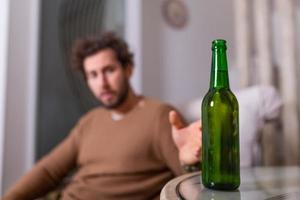 hombre alcohólico buscando una botella de cerveza, hombre bebiendo solo en casa. alcoholismo, adicción al alcohol y concepto de personas - alcohólico masculino con botella de cerveza bebiendo solo en casa foto