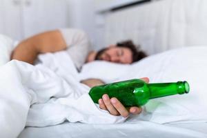 Unconscious drunk man with bottle of alcohol in hands sleeping in bed . Alcoholism problem and hangover concept photo