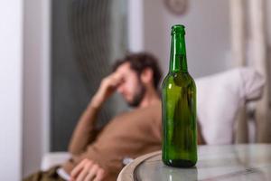 Silhouette of anonymous alcoholic person drinking behind bottle of alcohol. Man fighting with alcoholic habits, drink sitting on sofa at home photo