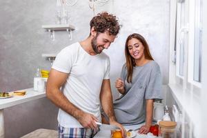 Female and male vegeterians stand together against kitchen interior, prepare fruit salad. Family couple cook on cozy kitchen, husband helps young wife to preapre breakfast for whole family. photo