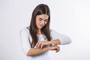 Young woman scratching her arm due to itching on a gray background. Female has an itching arm. The concept of allergy symptoms and healthcare photo