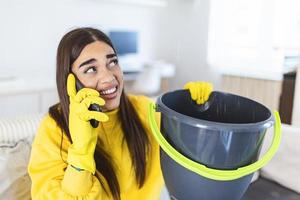 mujer sorprendida llamando a un plomero mientras recolectaba agua que se escapaba del techo usando un utensilio foto