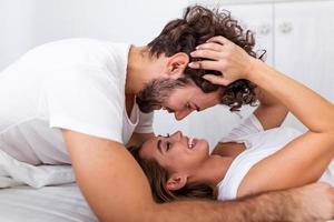 cariñosa joven pareja atractiva compartiendo un momento romántico en el dormitorio en casa. feliz pareja joven abrazándose y sonriendo mientras está acostado en la cama en un dormitorio en casa. foto