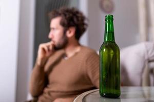 Silhouette of anonymous alcoholic person drinking behind bottle of alcohol. Man fighting with alcoholic habits, drink sitting on sofa at home photo