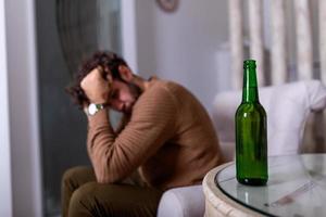 Depressed sad young addicted man feeling bad drinking beer alone at home, stressed frustrated lonely drinker alcoholic suffer from alcohol addiction having problem, alcoholism concept photo