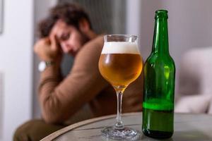 Depressed sad young addicted man feeling bad drinking beer alone at home, stressed frustrated lonely drinker alcoholic suffer from alcohol addiction having problem, alcoholism concept photo