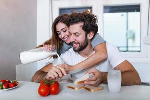 retrato de una pareja joven feliz cocinando juntos en la cocina de casa. linda pareja joven disfrutando de su desayuno juntos ella le está sirviendo leche mientras foto