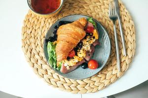 Fresh croissant sandwich with ham, scramble egg, tomato with tea on table, top view photo