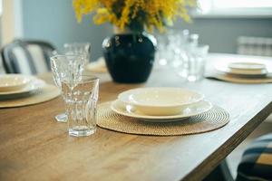 mesa de madera con platos y vasos vacíos. ajuste festivo de la mesa de pascua. ramas de mimosa en florero foto