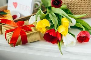 hermoso bouguet de flores tulipanes, paquete de caja de regalo, desayuno saludable con taza de café foto