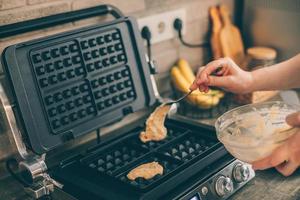 Young woman preparing Belgian waffles in the kitchen. Cooking process photo