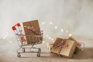 Concept of online shopping. Miniature shopping cart with gift box on desk. Copy space. photo