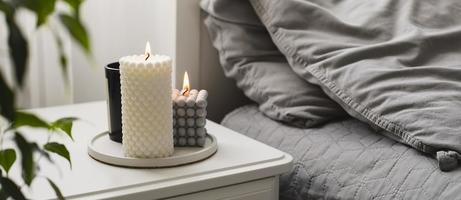 Modern burning candle on bedside table near bed. Home aroma. Wellness. Banner image for design photo