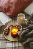 Burning candle with wooden wich in amber glass gar, open book and cup of coffee or tea. Autumn home decor. photo