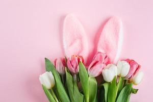 Fluffy bunny ears and tulips flowers on pink background. Easter holiday concept. Top view, flat lay photo