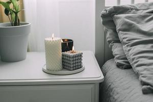 Bedside table near bed in bedroom with burting candles. Concept of cozy aroma home, wellbeing photo