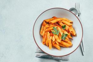 pasta penne con salsa de tomate en plato blanco sobre mesa de fondo de piedra. vista superior, espacio de copia foto