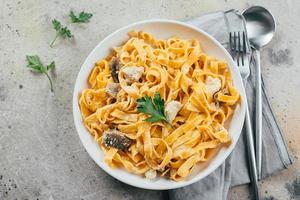 Italian pasta fettuccine alfredo with chicken, mushrooms and sause on plate on stone table. Top view photo