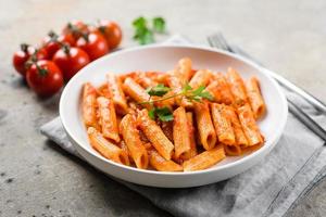 Penne pasta with tomato sause in white plate on stone background table. Closeup. Italian food photo