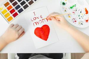 feliz día de la madre. niña dibujando una tarjeta hecha a mano para mamá para las vacaciones con acuarelas. foto