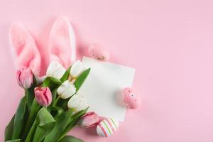 Easter background with easter eggs, fluffy bunny ears, spring tulips and empty card for text. Mockup. photo